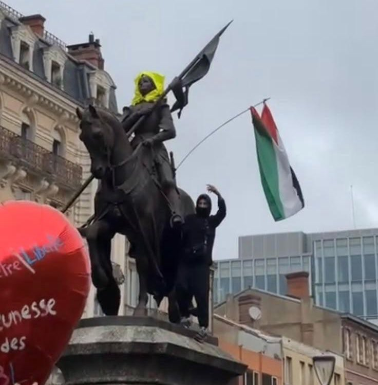 A masked protester waves a Palestinian flag atop an equestrian statue