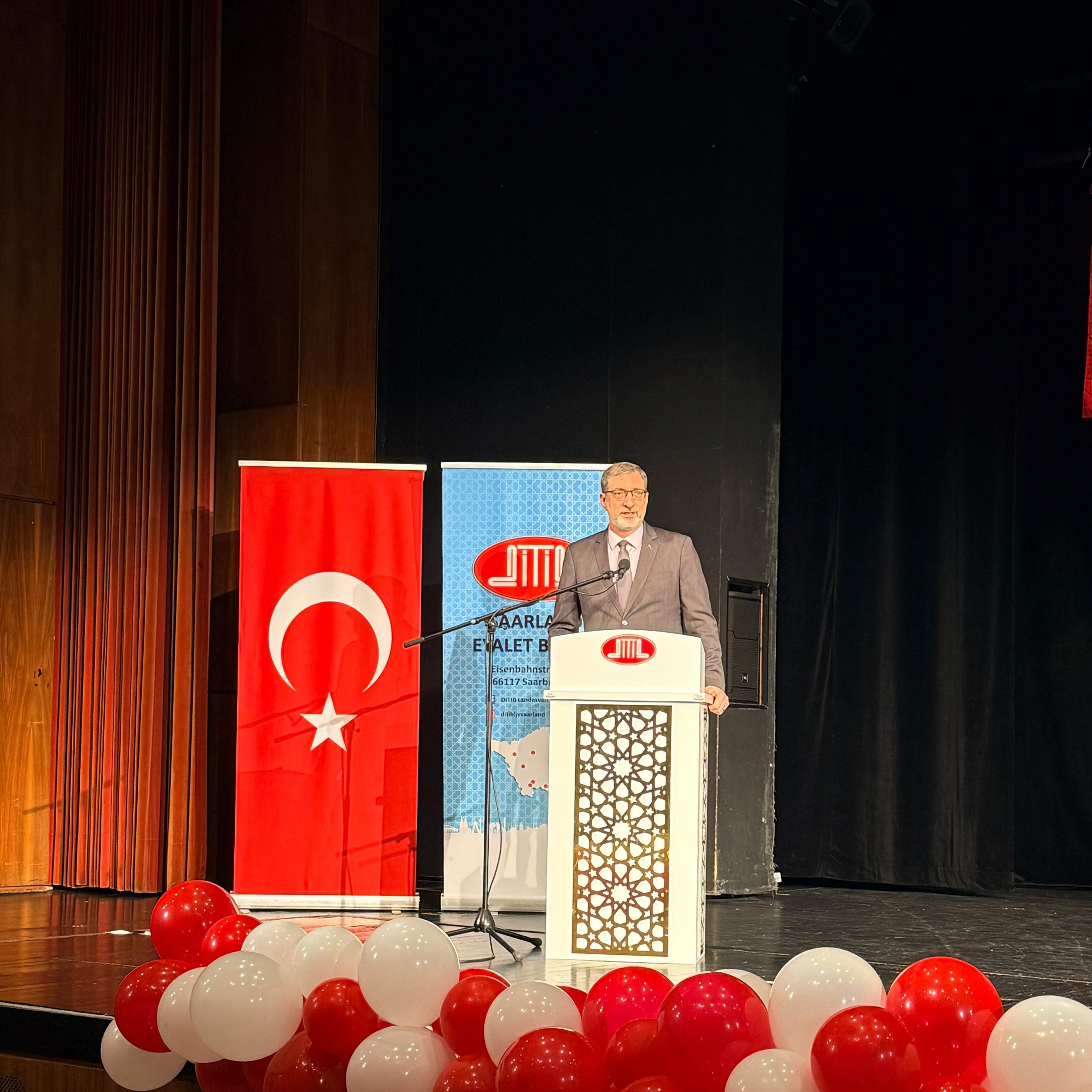 A speech delivered at the podium in front of a Turkish flag and DİTİB banner at the event in Merzig