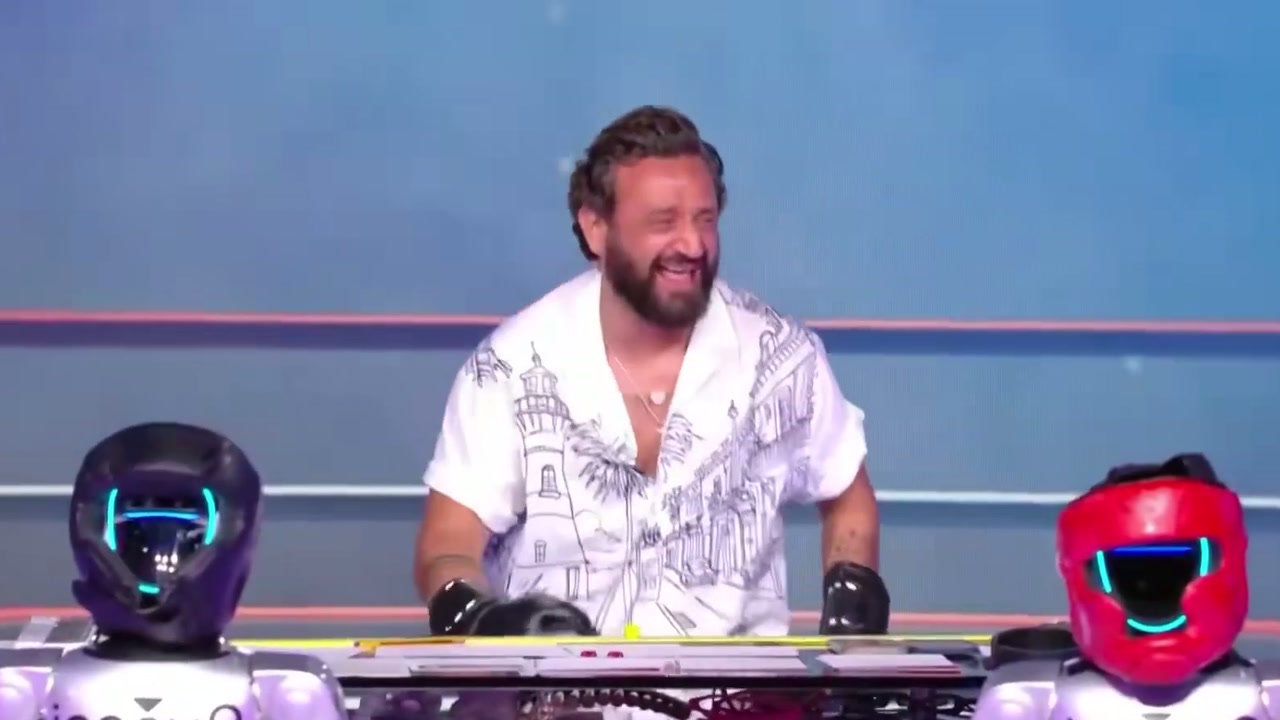 Hanouna, dövüşün ardından iki boksör robotun arasında gülüyor (Haziran 2026)