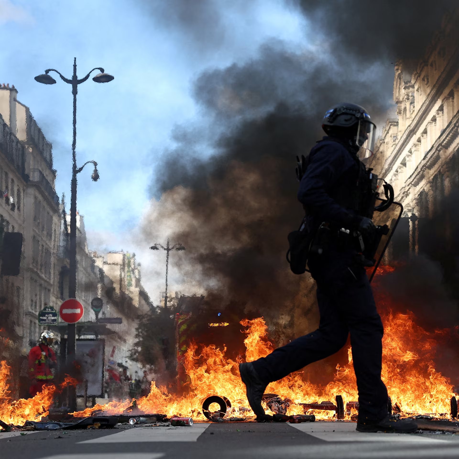 Paris'teki protestolarda yanan barikatların önünden geçen bir polis